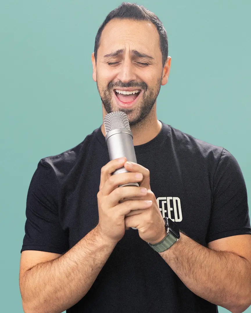 Achi in a FEED t-shirt passionately singing into a handheld microphone.