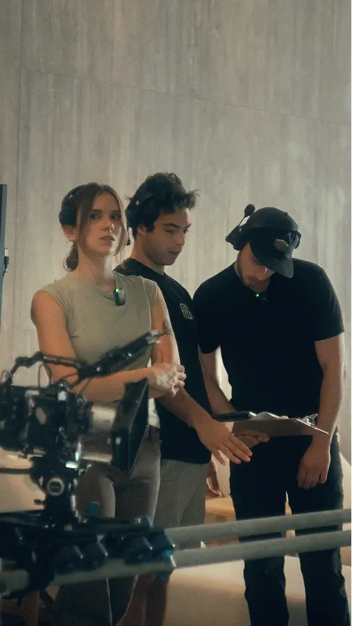 Emma, Anthony, and Ben on a set reviewing the footage next to professional camera equipment.