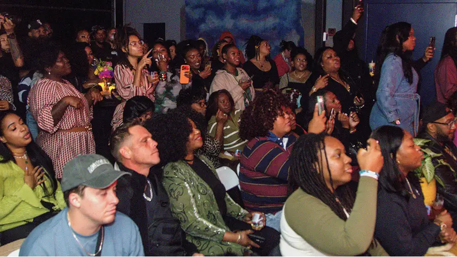 Audience watching and recording an event in The CAVE Studio, with some holding drinks and phones.