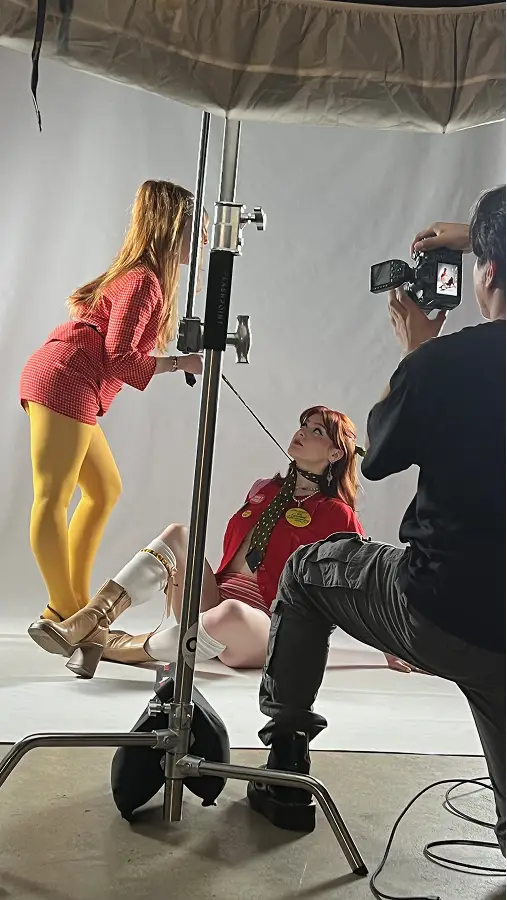 Photography session with two women in retro outfits posing against a white backdrop while a photographer captures the scene.