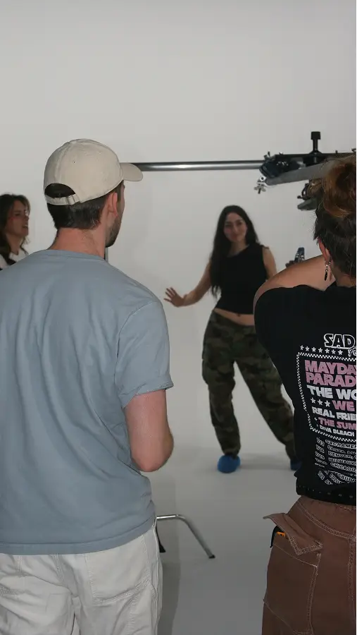 Team in The CAVE Studio; a woman in camo pants poses while others observe and photograph her.