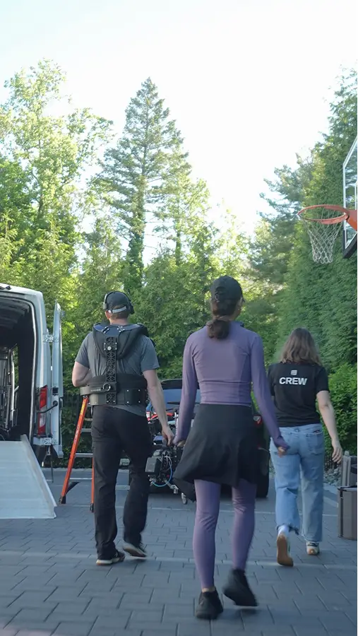Team walking on a set; a paved driveway with trees and a basketball hoop in the background.