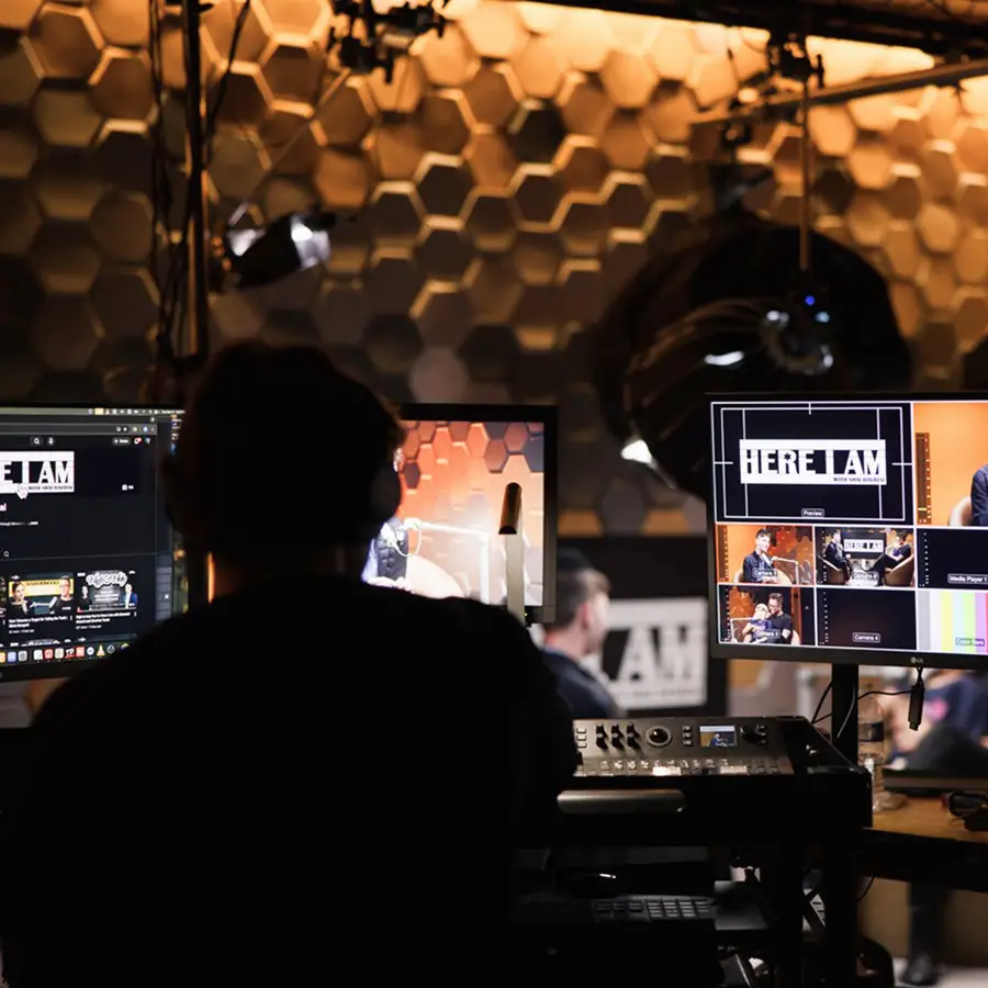 Person with headphones operating video production equipment with multiple monitors showing a live recording in The CAVE Studio.