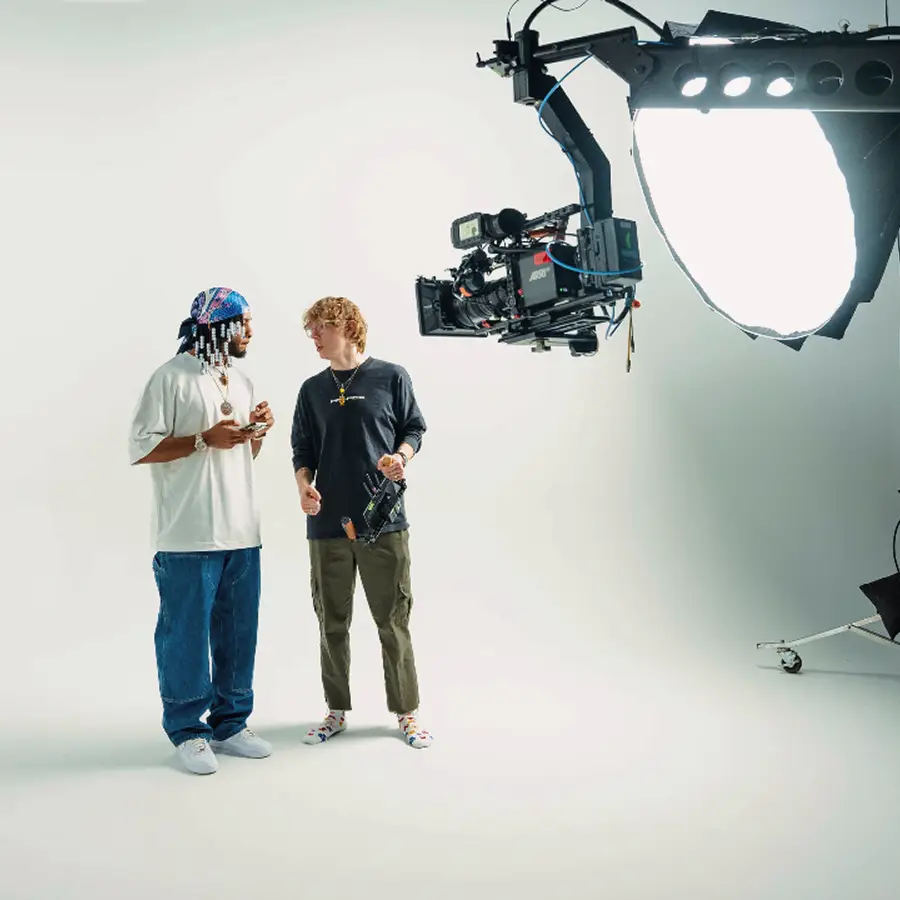 Two men standing and talking on a set in The CAVE Studio with a large camera crane and bright studio lighting.