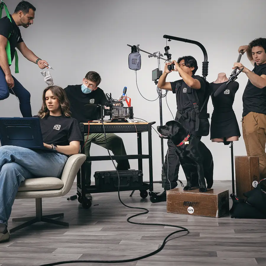 Crew working in The CAVE Studio with equipment, including camera, lights, a black dog on a box, and a mannequin in black dress.