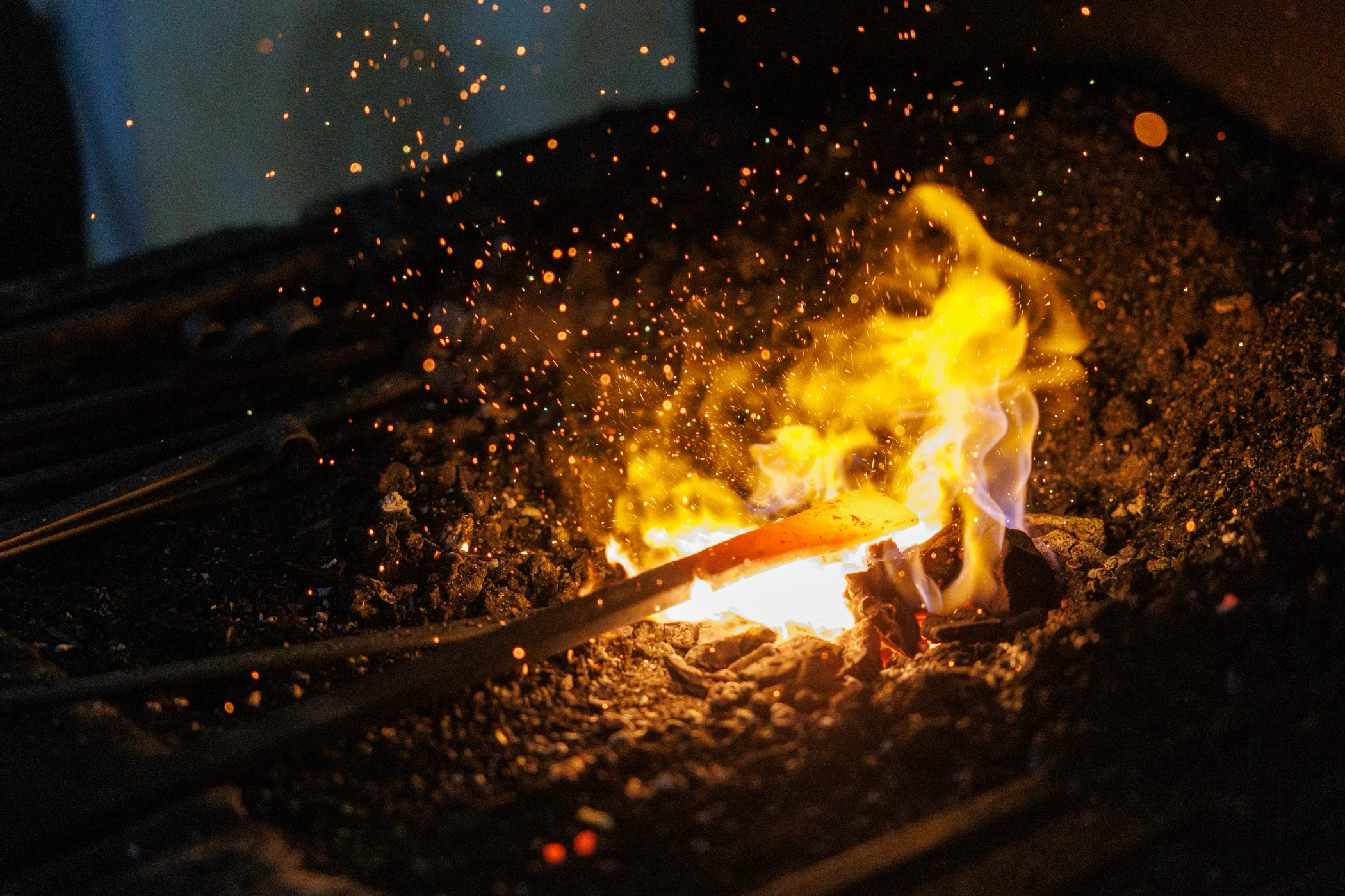 Glowing metal piece heated in a blacksmith's forge surrounded by sparks and flames.