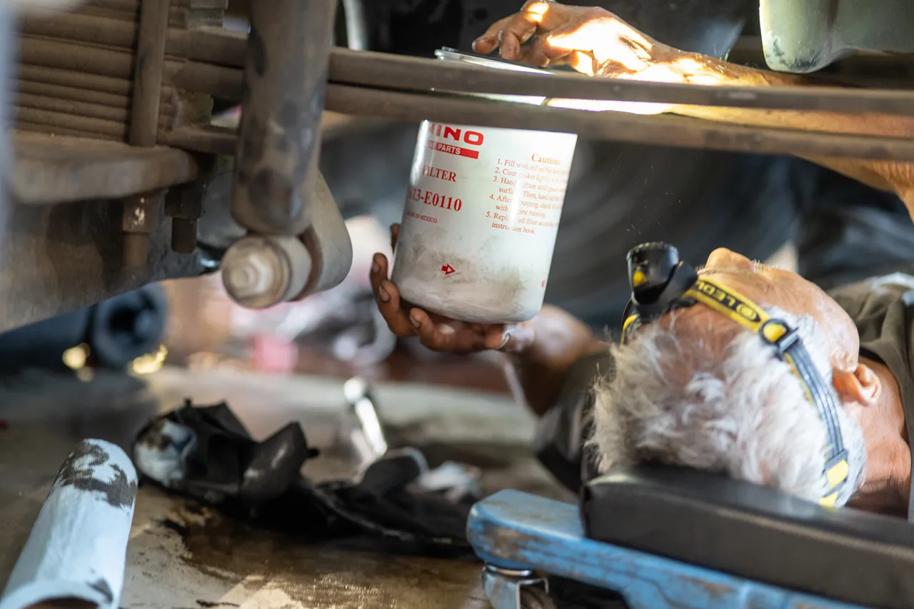 Technician installs an Oil filter labeled HINO beneath a heavy-duty truck chassis during service.