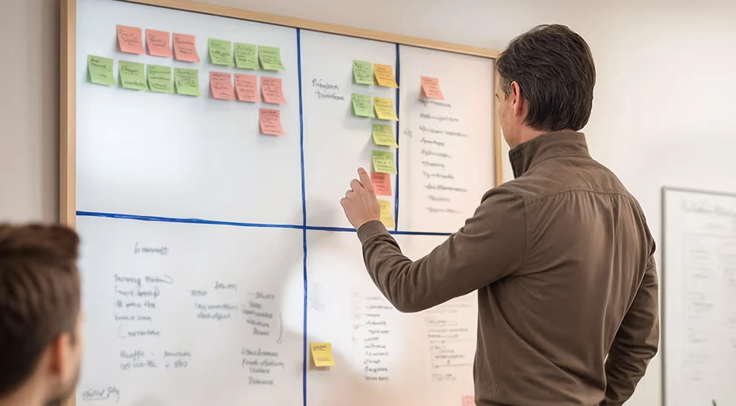 A man gestures towards a whiteboard filled with various sticky notes, indicating a collaborative discussion.