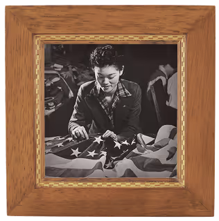 Black and white photo of a woman sewing an American flag, framed in a wooden frame.