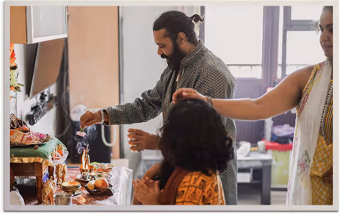 Man performing a Hindu prayer ritual with incense and offerings while two women participate nearby.