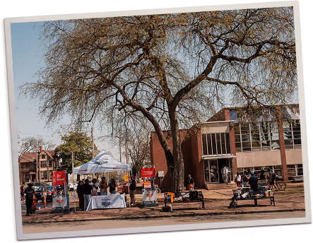 Volunteers outdoors distributing food and supplies under a canopy with trees in the background.