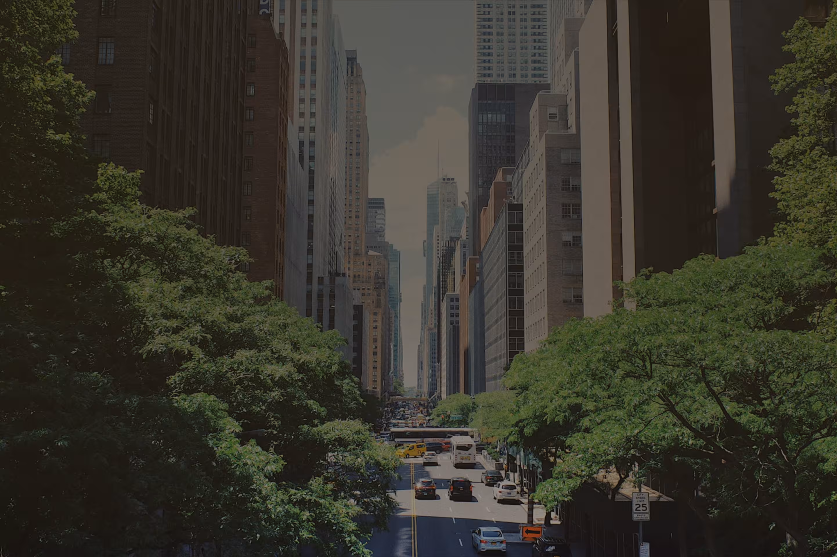 Street view of a busy city avenue lined with tall buildings and green trees along both sides.