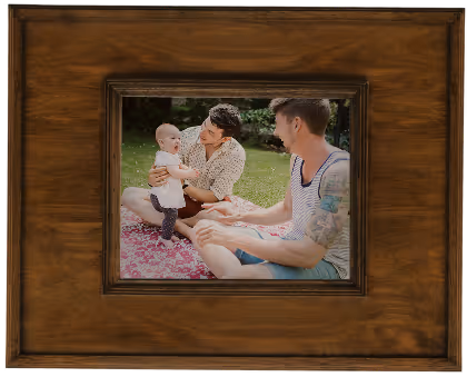 Framed photo of two men sitting on a picnic blanket outdoors, one holding a baby.
