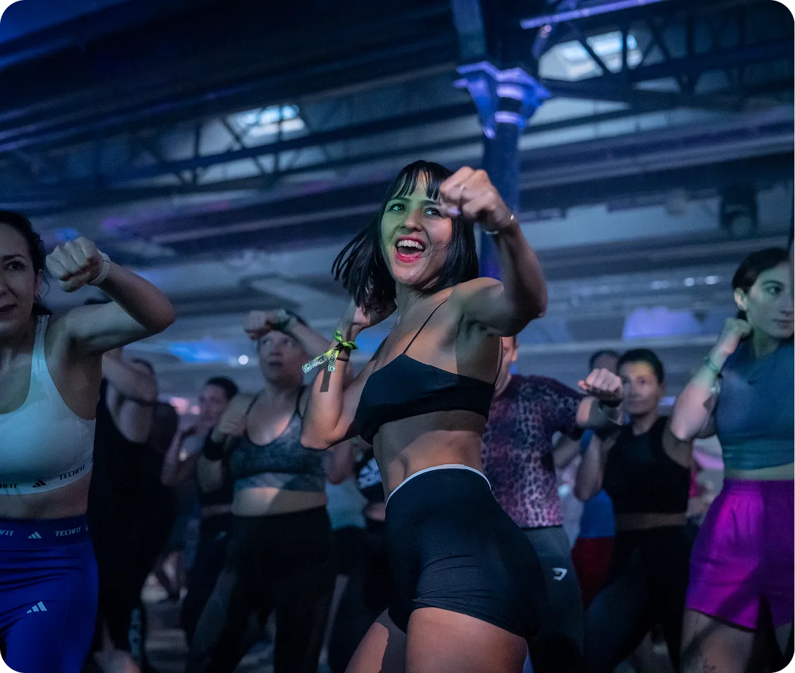 Group of people in athletic wear energetically boxing in a gym with a smiling woman in the foreground.