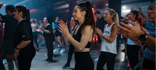 Group of people clapping and participating in a fitness class inside a gym.