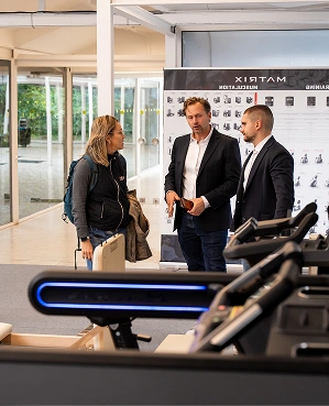 Three people having a conversation indoors near gym equipment, with a banner in the background.