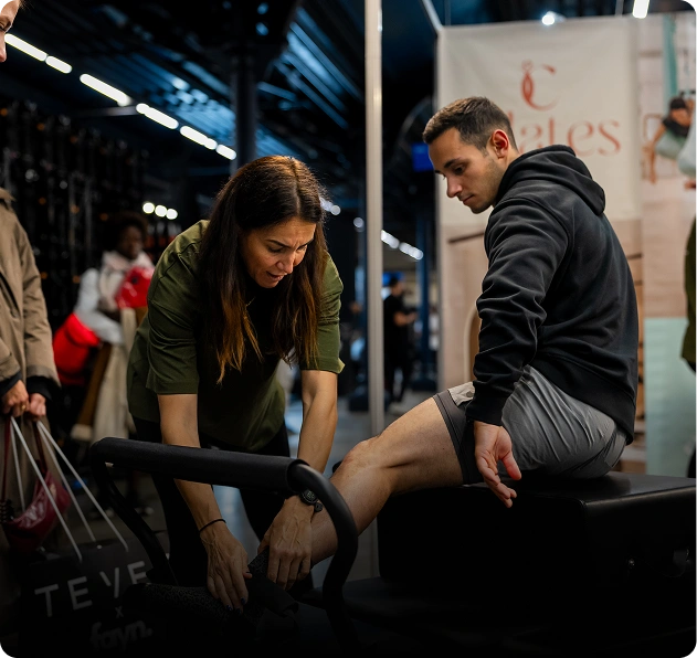 A woman fitting a shoe on a seated man's foot in a brightly lit indoor setting.