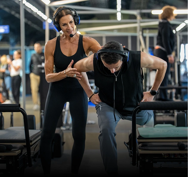 Female fitness coach wearing a headset guiding a man doing dips exercise on parallel bars in a gym.