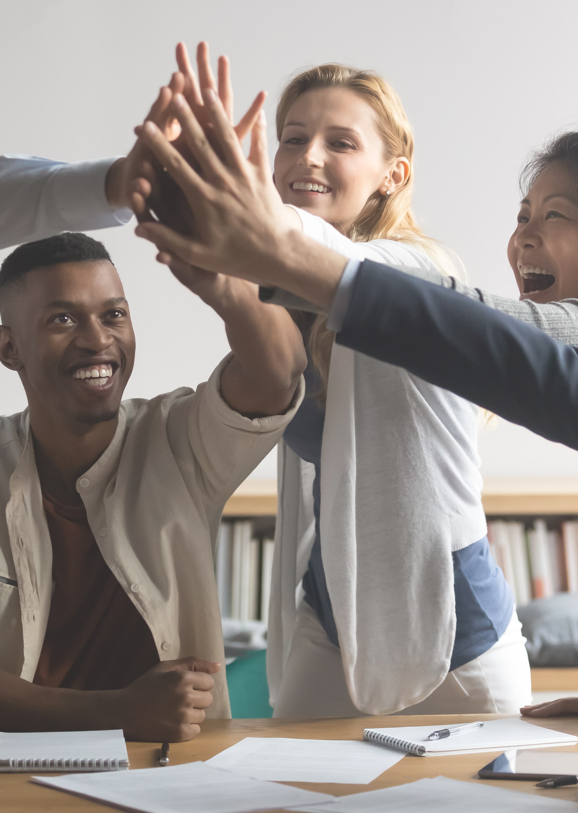 A diverse group of cheerful colleagues giving a group high five in an office setting.