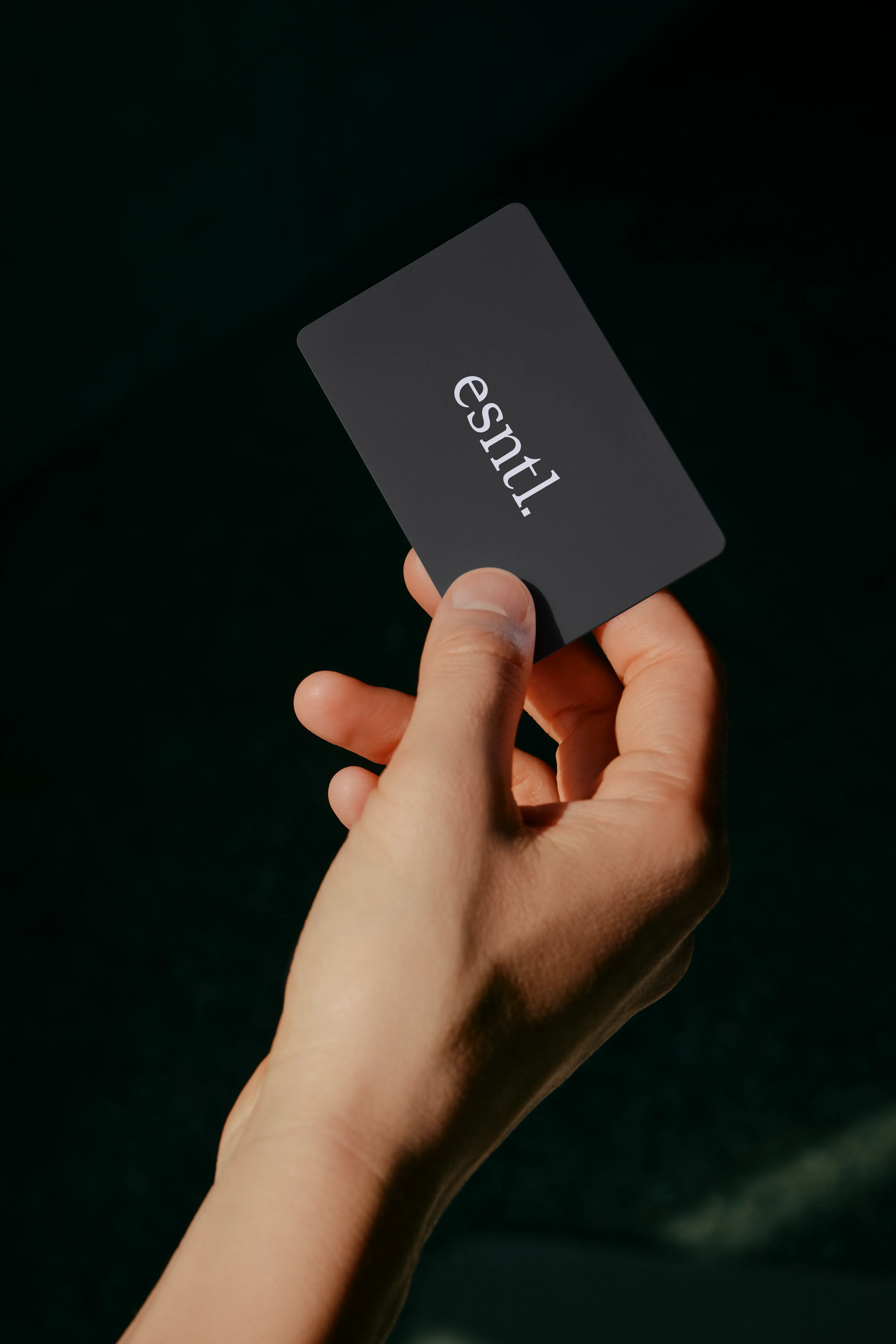 Hand holding a black card with the word 'esntl.' in white letters.