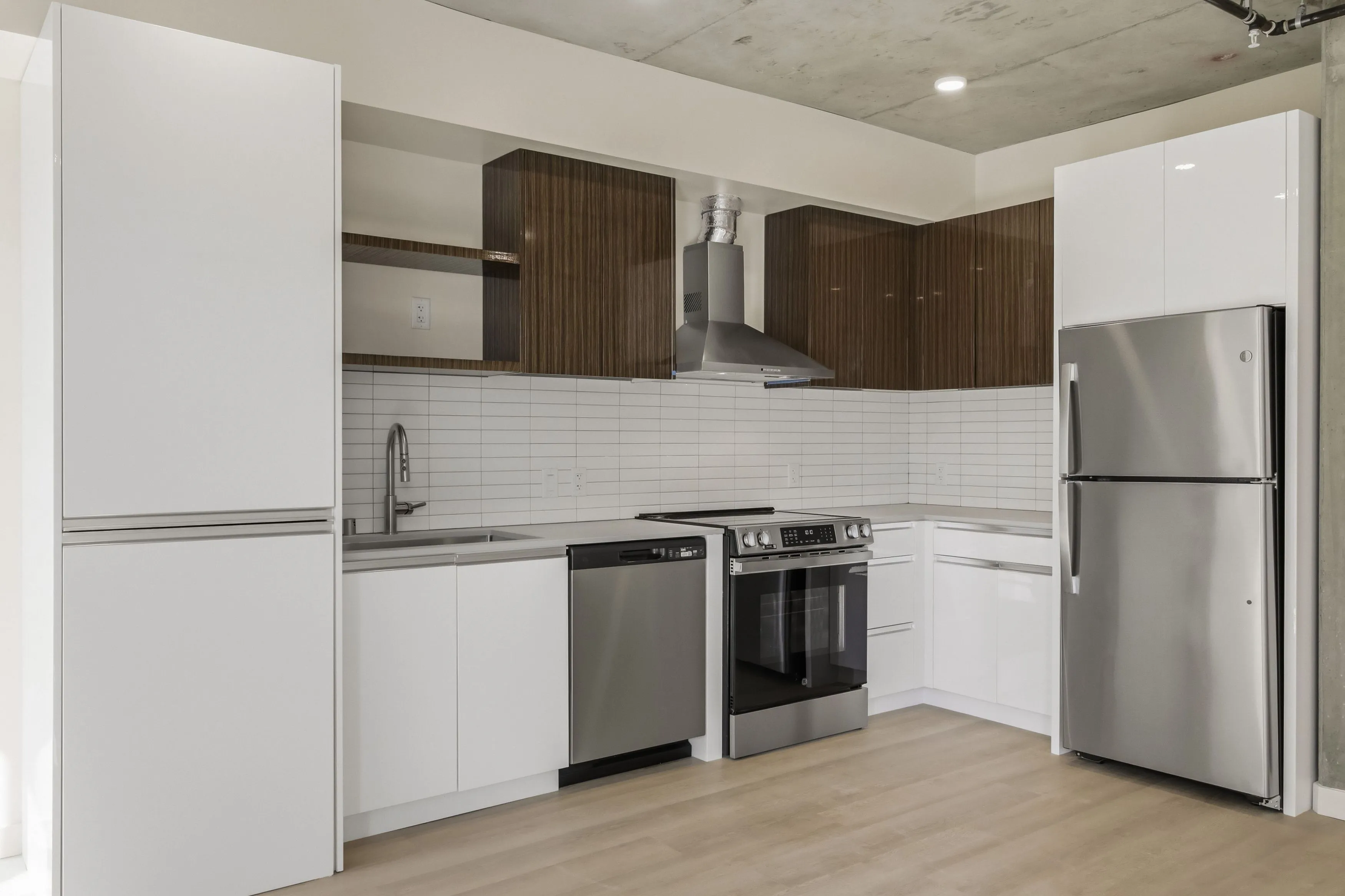 Modern kitchen with white lower cabinets, wood-finish upper cabinets, stainless steel appliances including a refrigerator, oven, dishwasher, and a range hood.