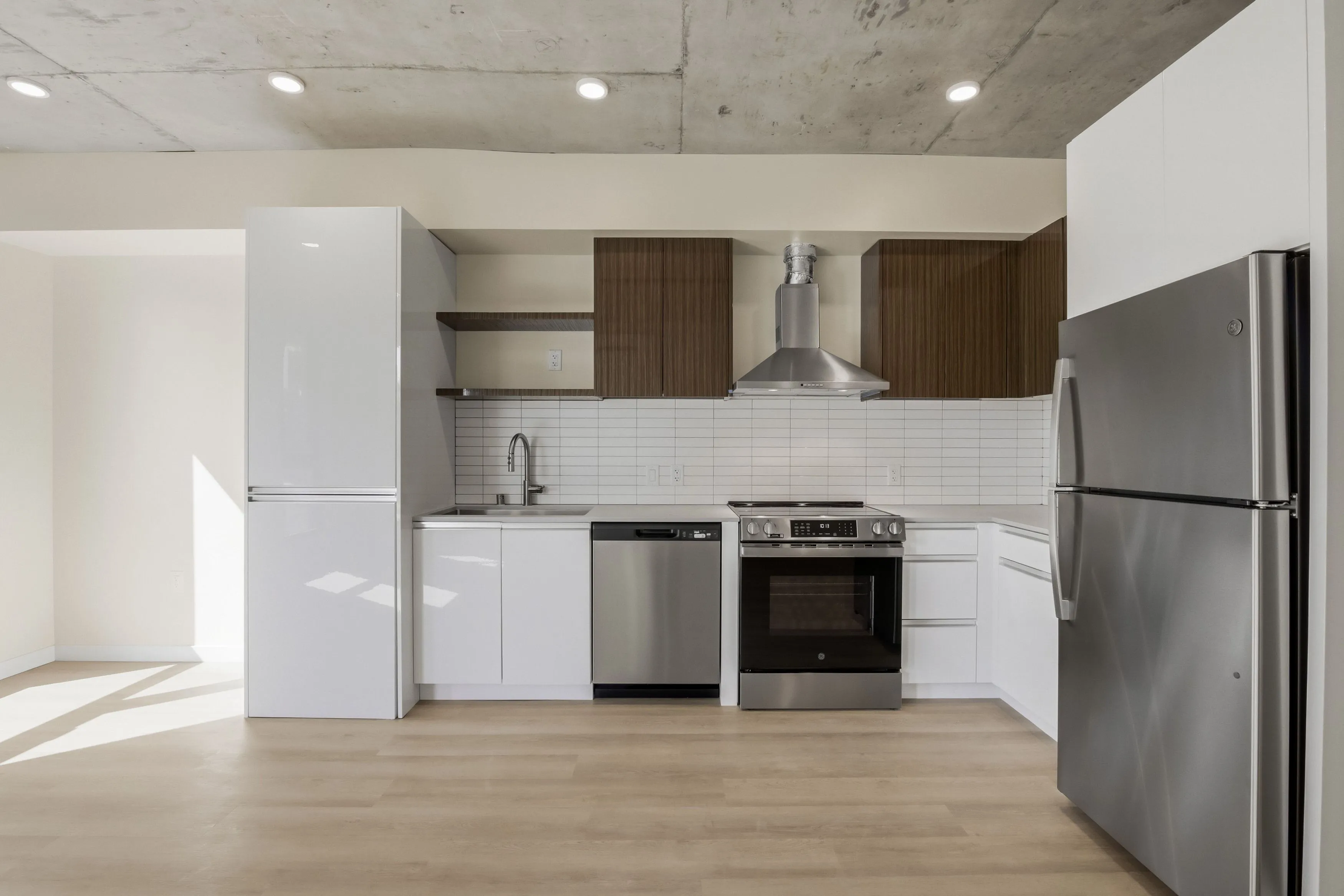 Modern kitchen with white cabinetry, wood upper cabinets, stainless steel appliances including refrigerator, oven, and dishwasher, and a subway tile backsplash.