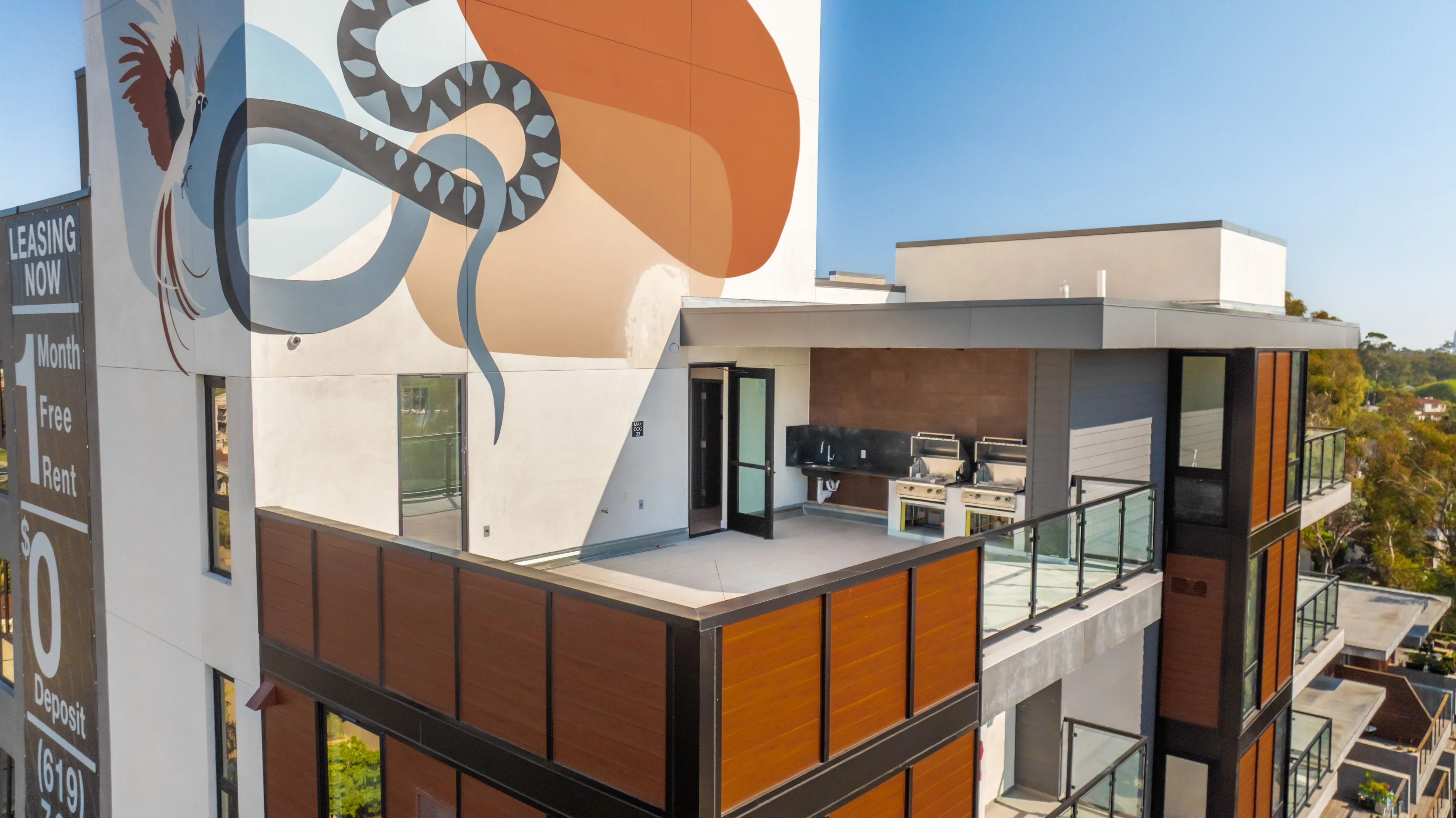 Modern apartment building balcony with outdoor grills and a large colorful mural on the adjacent wall.