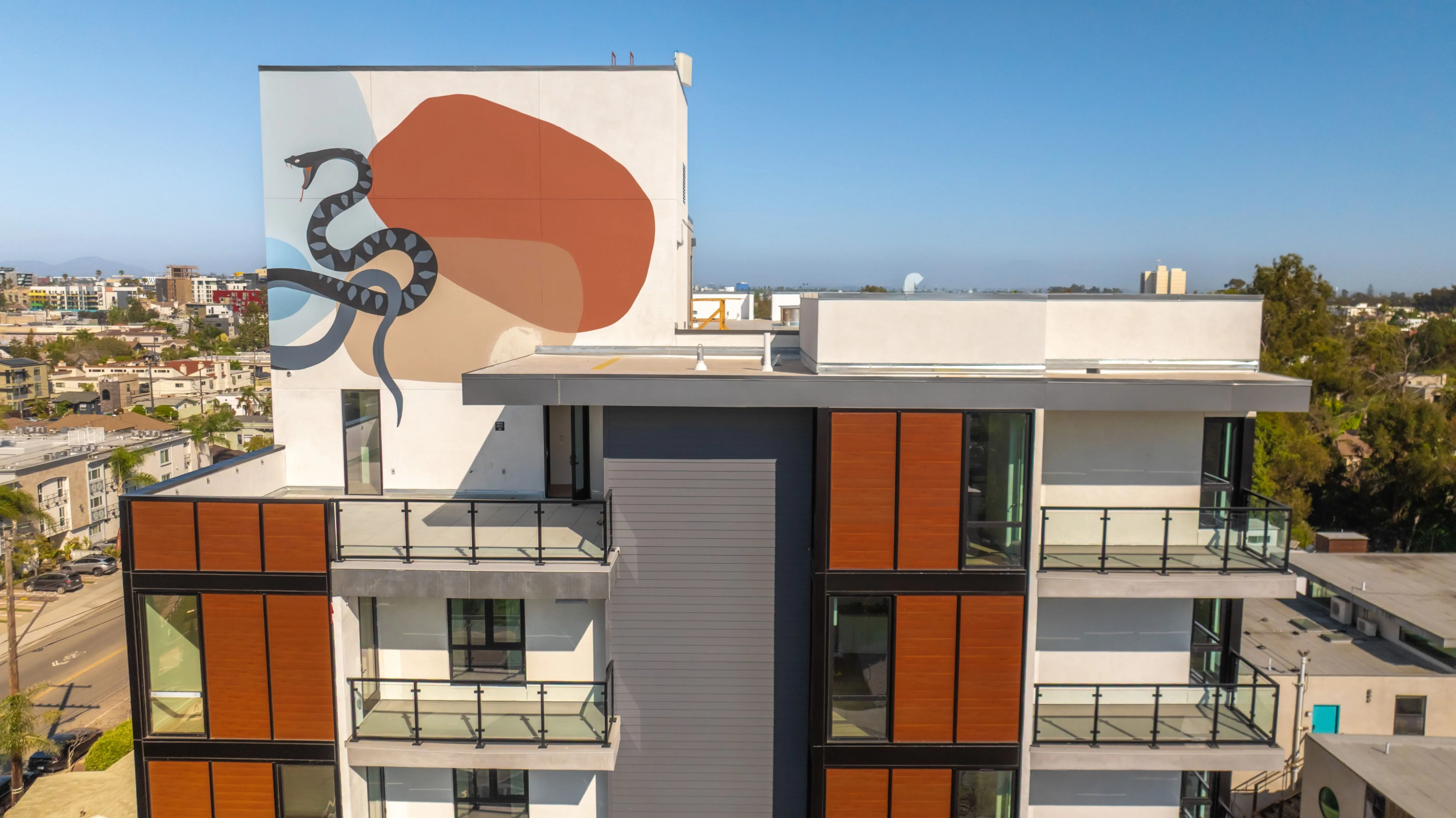 Modern multi-story building with balconies and a large mural of a black snake on abstract color shapes on the upper wall.