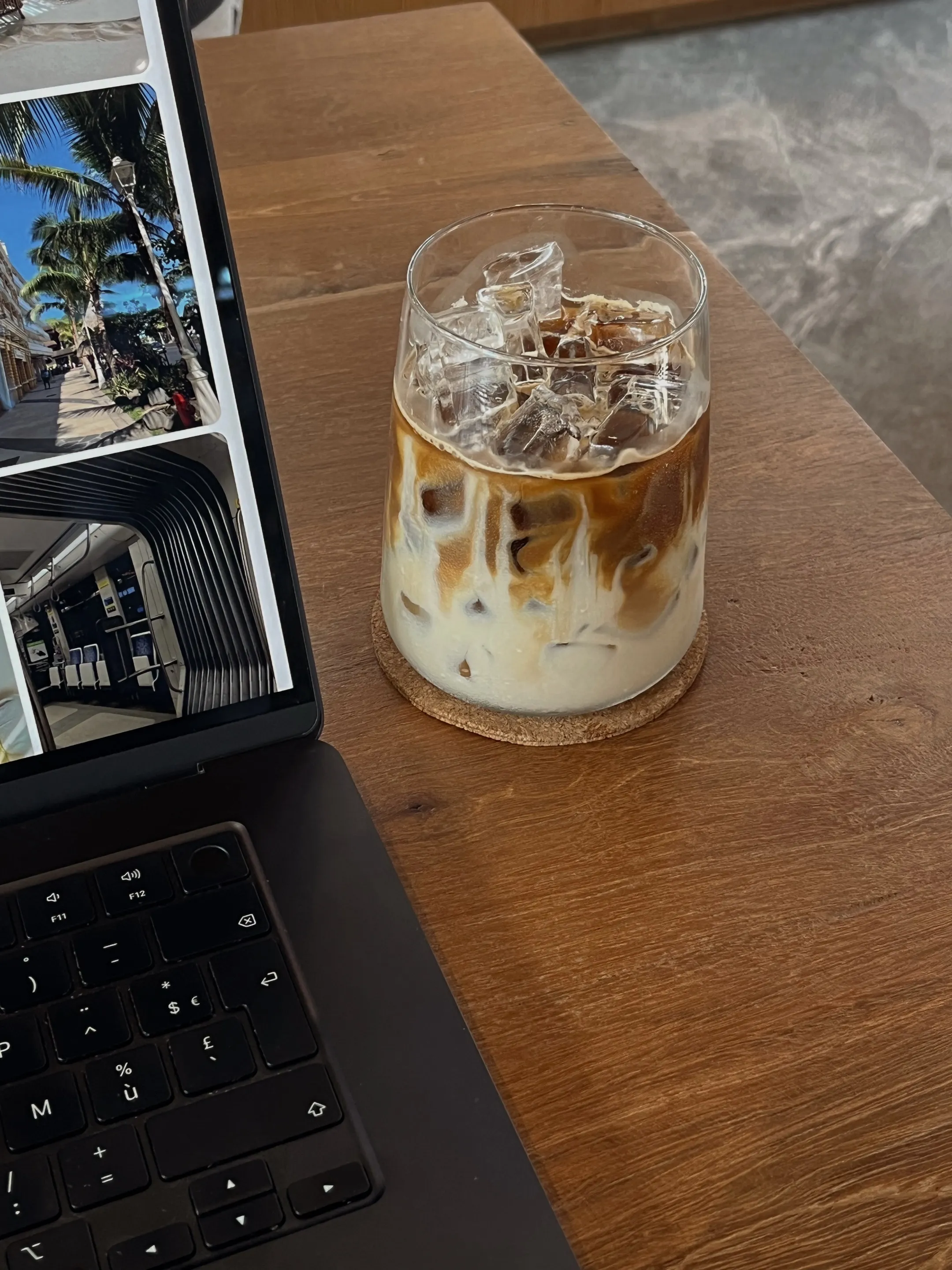 Glass of iced coffee with milk on a wooden table next to a laptop keyboard.