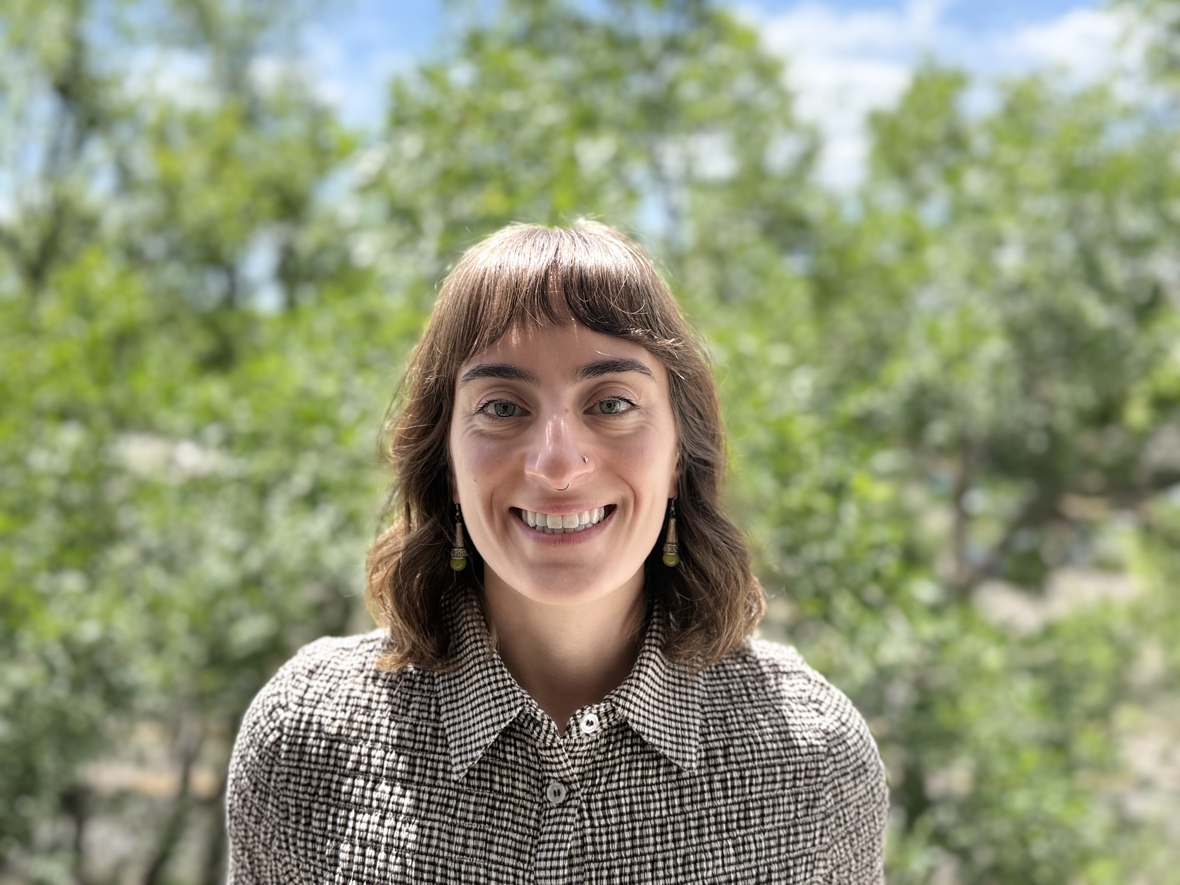 Headshot of a girl with brown hair, wearing a blue sweater, smiling in front of a brick wall