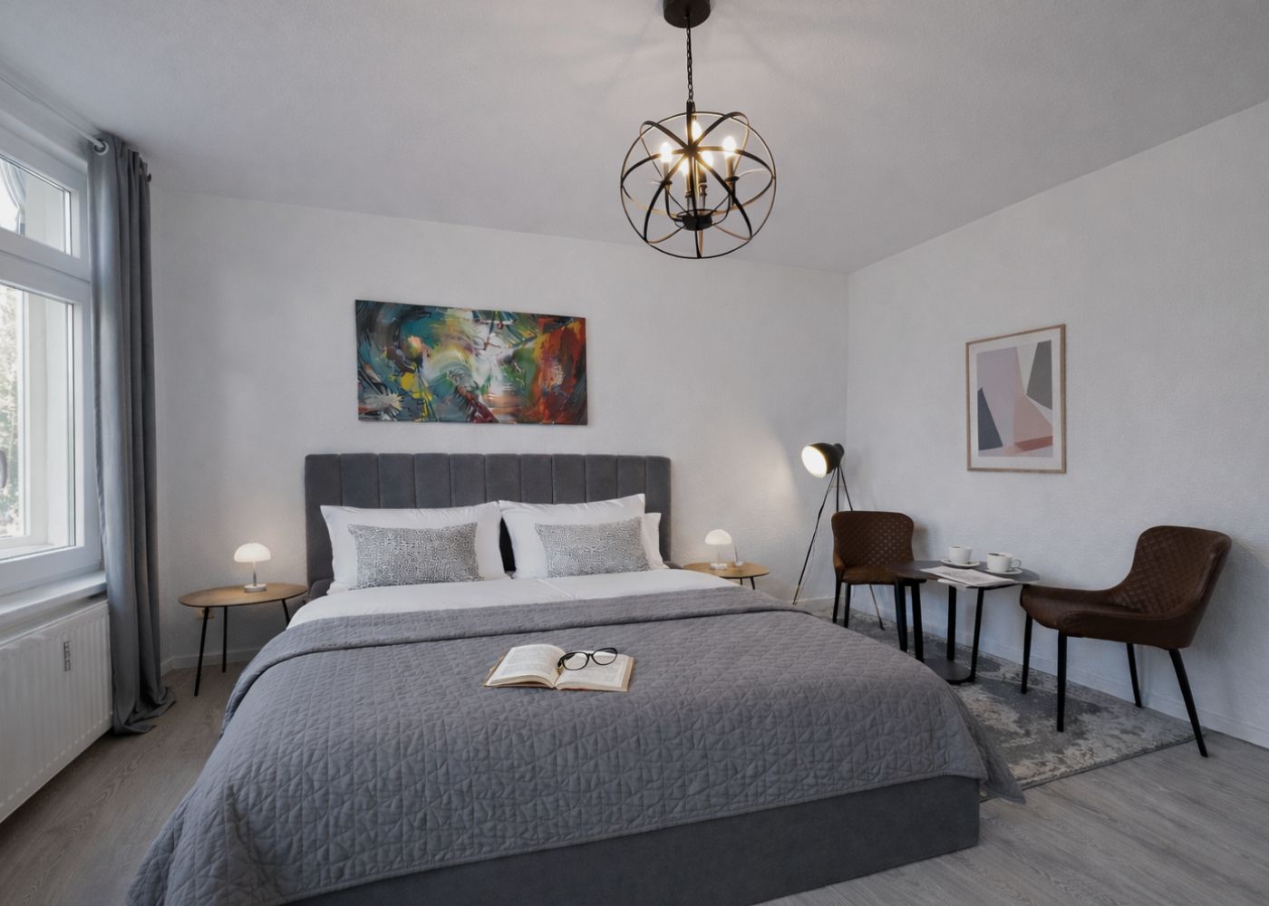 Schlafzimmer mit Doppelbett, grauer Tagesdecke, weißen Handtüchern und stilvollen Wandbildern – gemütlich und modern eingerichtet