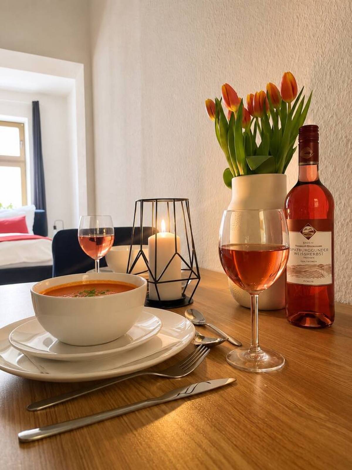 Gedeckter Esstisch mit Suppe, Weingläsern und orangefarbenen Tulpen
