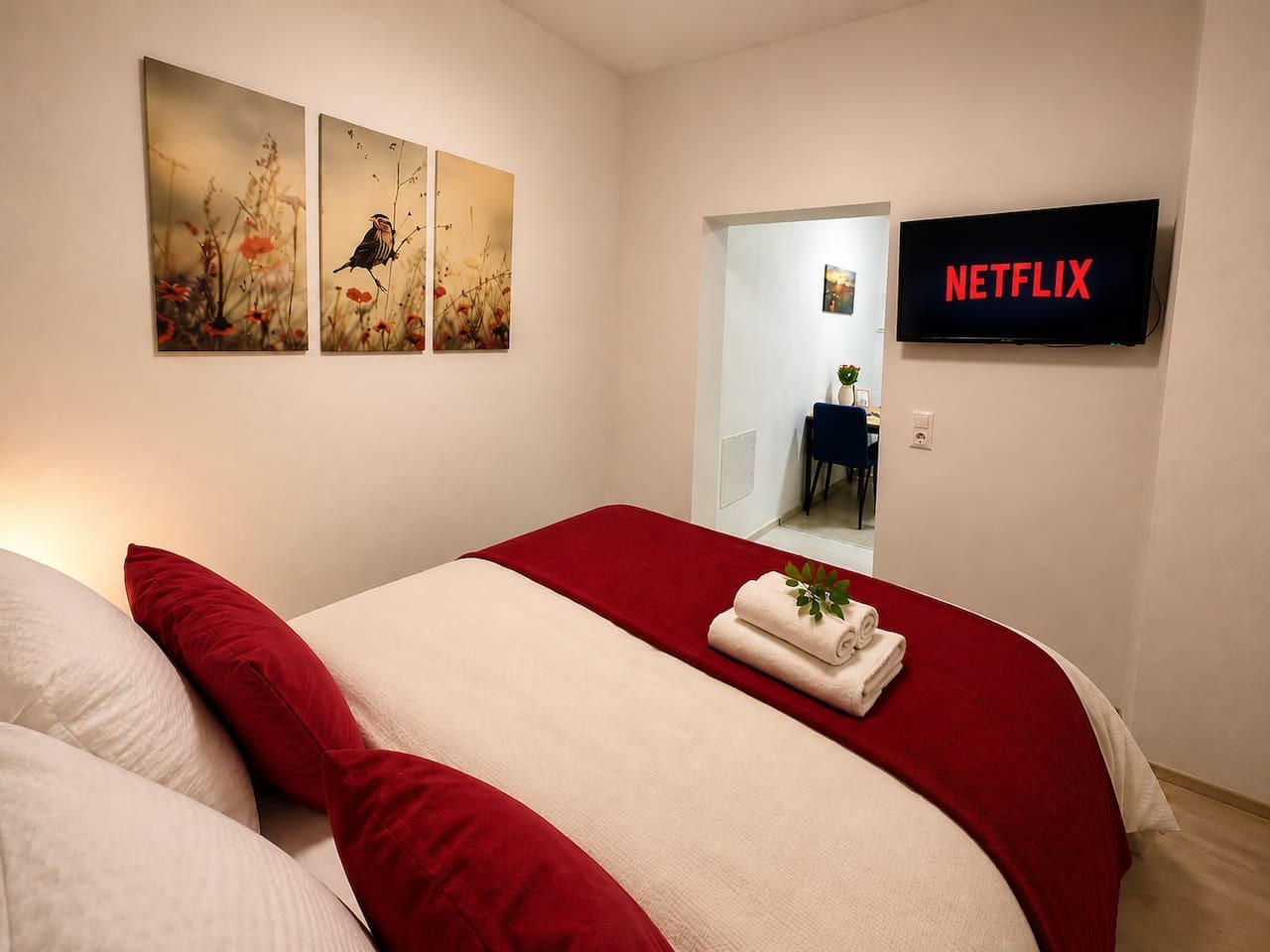 Doppelbett mit roter Tagesdecke und wandmontiertem Fernseher