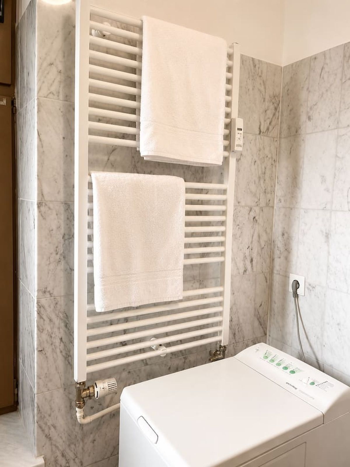 Badezimmer mit Handtuchheizkörper, weißen Handtüchern und Waschmaschine