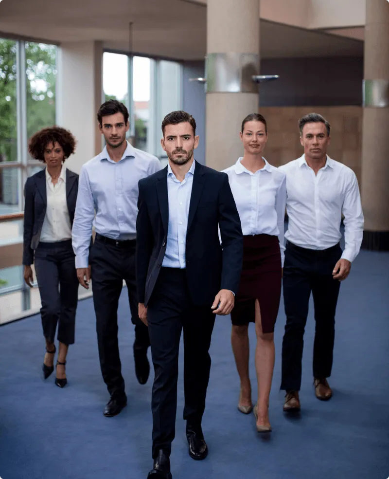 Five business professionals confidently walking forward in a modern office corridor.
