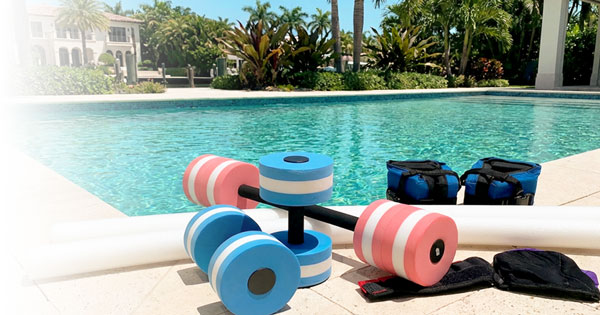 Aqua fitness equipment including water dumbbells, foam noodles, and resistance weights placed at the edge of a swimming pool for water workouts