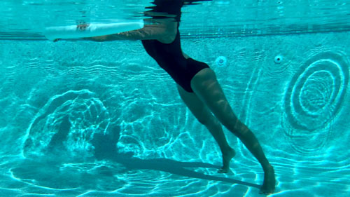 Woman performing a pool pilates lat pull, pressing a noodle down from a diagonal position.