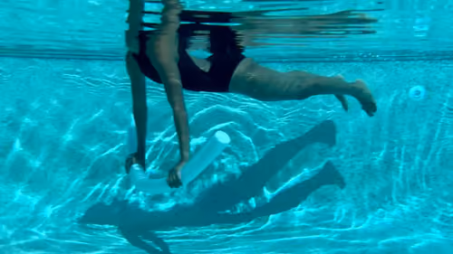 Woman holding a plank position in the water using a noodle in a pool pilates exercise.