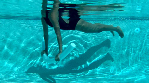 Woman holding a plank position in the water using a noodle in a pool pilates exercise.