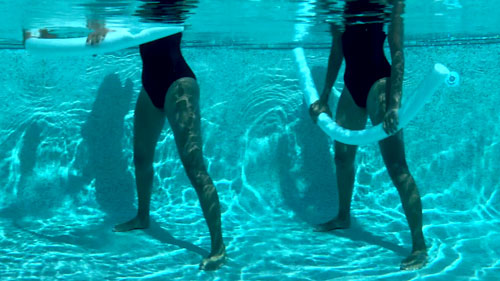 Woman performing a pool pilates chest expansion, pressing a noodle down and controlling the lift.