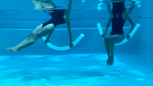Woman performing a pool pilates reverse plank, lifting and lowering on a noodle.