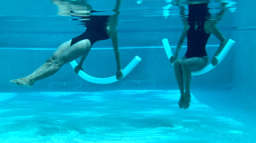 Woman performing a pool pilates reverse plank, lifting and lowering on a noodle.