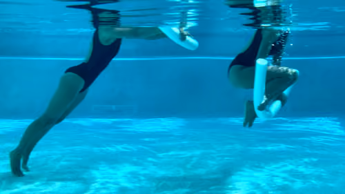 Woman performing a pool pilates reverse crunch, tucking knees in and extending out with a noodle.
