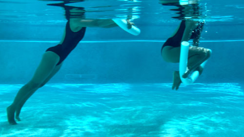 Woman performing a pool pilates reverse crunch, tucking knees in and extending out with a noodle.