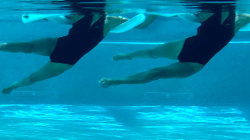 Woman performing a pool pilates walking exercise, alternating legs forward and back with a noodle.