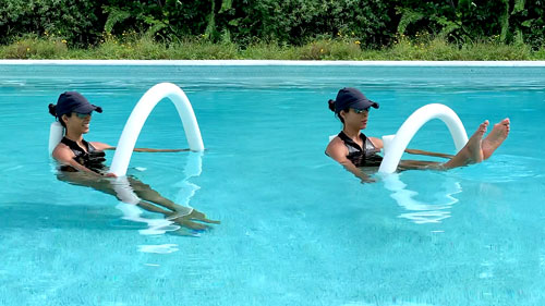 Woman performing a pool pilates teaser, lifting and lowering the legs with a noodle.
