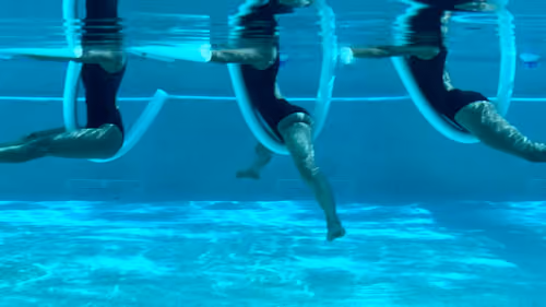 Woman performing pool pilates leg circles, moving legs through a full range with a noodle.