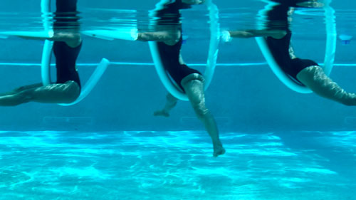 Woman performing pool pilates leg circles, moving legs through a full range with a noodle.