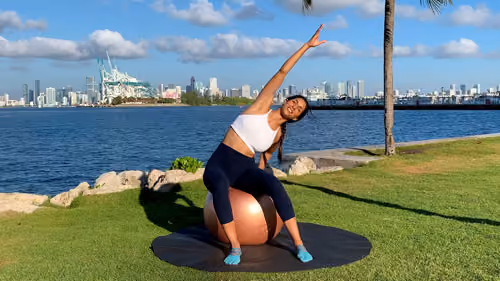 Side stretch on a stability ball reaching overhead to lengthen the torso and improve flexibility