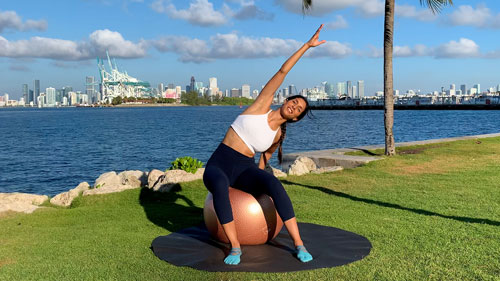 Side stretch on a stability ball reaching overhead to lengthen the torso and improve flexibility